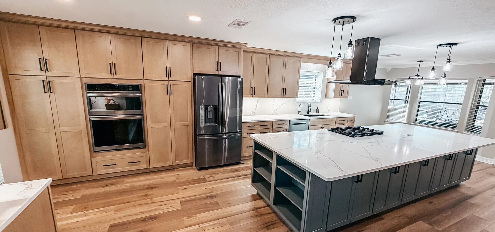 Open-concept kitchen with a large quartz island, custom range hood and wood floors from a full home remodel in Manvel, TX